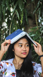 Portrait of young woman holding plant against trees