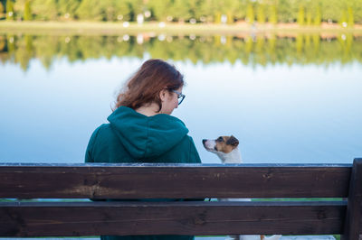 Rear view of woman sitting on bench with dog against lake