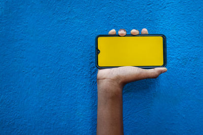 Close-up of hand holding yellow paint against blue wall