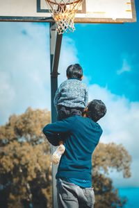 Rear view of boy standing against blue sky