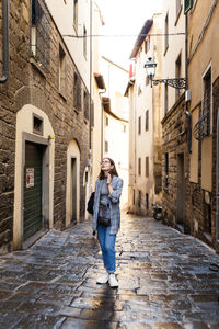 Full length of woman standing on alley amidst buildings in city