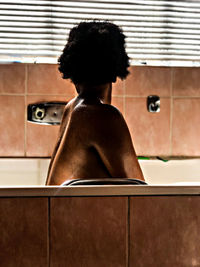 Rear view of shirtless man sitting in bathroom