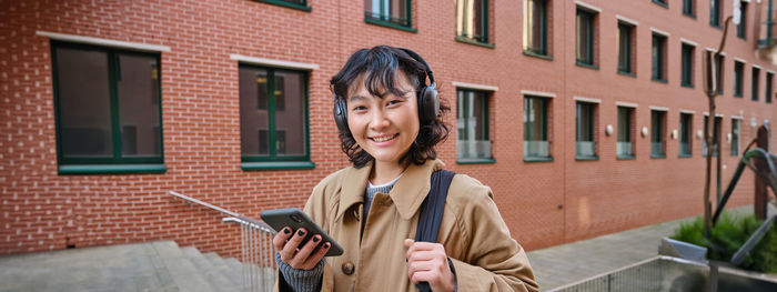 Portrait of young woman standing against building