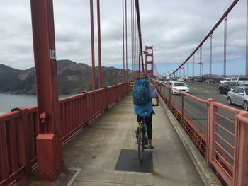 Rear view of man riding bicycle on bridge against sky