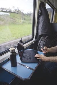 Cropped hands of man using laptop in train