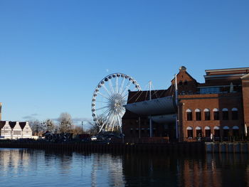Ferris wheel by buildings against clear blue sky