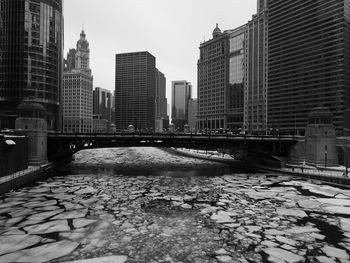 Bridge over river amidst buildings in city against sky