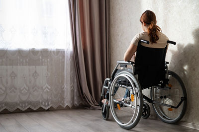 Rear view of disable woman sitting on wheelchair at home