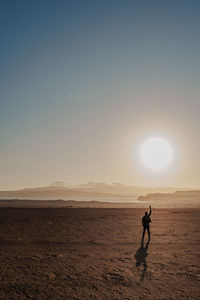 Silhouette woman walking at beach against sky during sunset