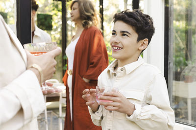 Smiling boy holding drink while looking at mother during back yard party