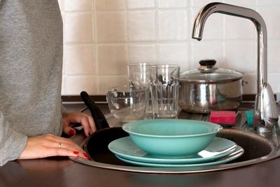 Midsection of woman cleaning plates in kitchen at home