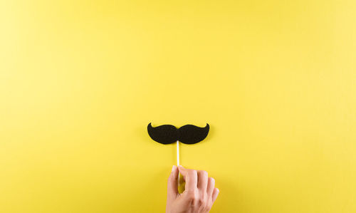 Close-up of hand holding umbrella against yellow background