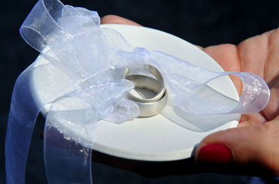 Cropped hand of woman holding wedding rings with white ribbons