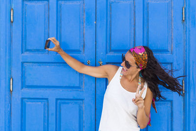 Smiling woman taking selfie while standing against closed door of house