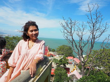 Smiling young woman standing by sea against sky