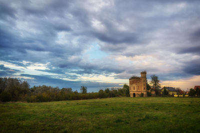 Abandoned building in field against cloudy sky