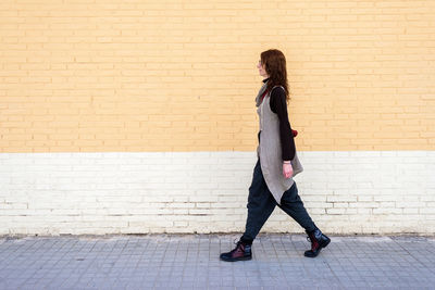 Young beautiful woman with eyeglasses walking against bricked wall .