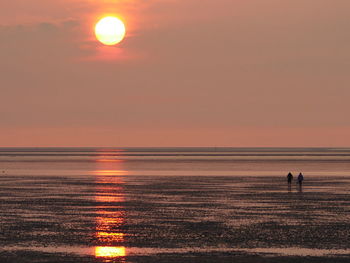 Scenic view of two people walking on wet beach at sunset