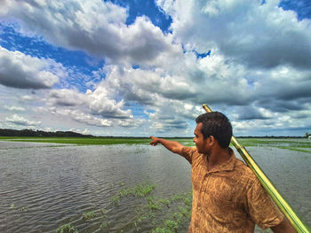 Rear view of man standing by lake against sky