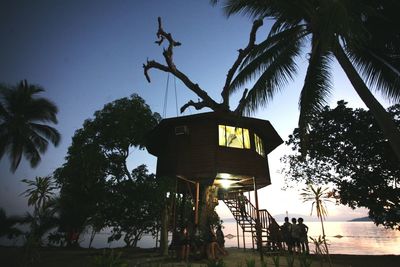 People by tree house at beach during sunset