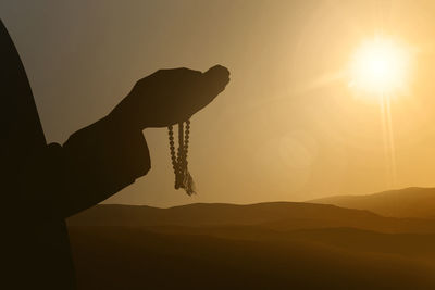 Silhouette person holding sun against sky during sunset