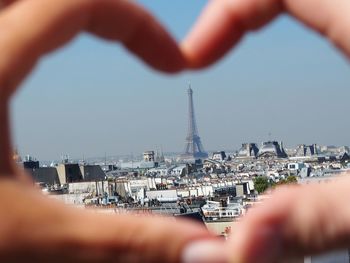 Cropped image of hand holding cityscape against sky