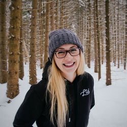 Portrait of smiling young woman standing at forest during winter