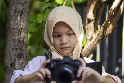 Portrait of a smiling asian muslim girl holding digital camera.outdoors
