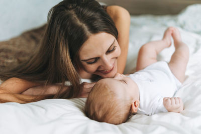 Young mother having fun with cute baby girl on bed, natural tones, love emotion