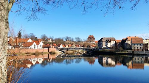 Reflection of buildings and trees in river against clear blue sky