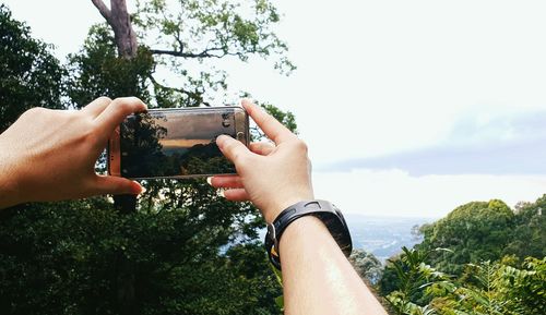 Midsection of man using mobile phone against sky