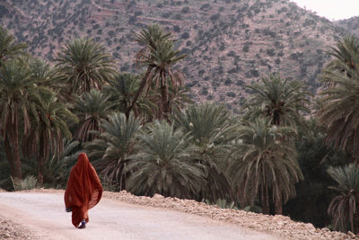 Rear view of woman walking on road against trees