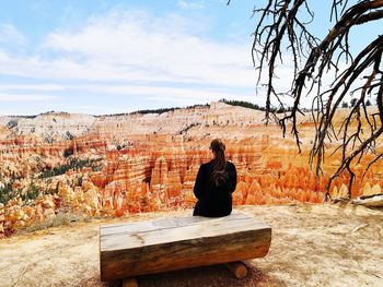 Rear view of woman sitting on bench against sky