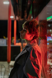 Pensive woman against glass wall on the street with red neon light at night. sad and loneliness.