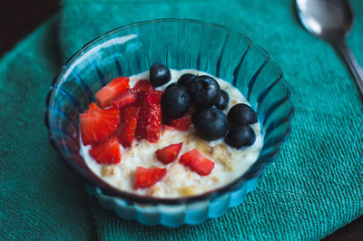 Cooked oat with forest fruits. strawberries and blueberries in a blue glass bowl on a green napkin.