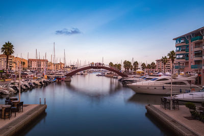 Boats moored at harbor against sky in city