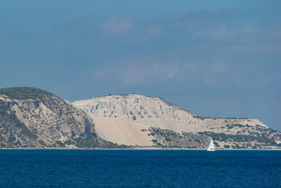 Scenic view of sea by mountain against sky