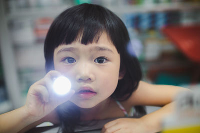 Close-up portrait of girl holding illuminated flashlight at home