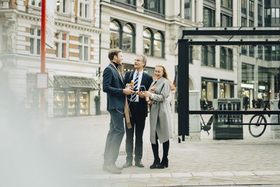 Smiling male and female business colleagues talking while standing in city