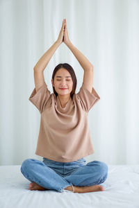 Full length of woman meditation on bed at home