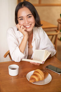 Portrait of young woman using mobile phone while sitting on table