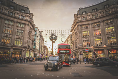 Cars on city street by buildings against sky