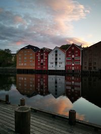 Buildings by lake against sky during sunset