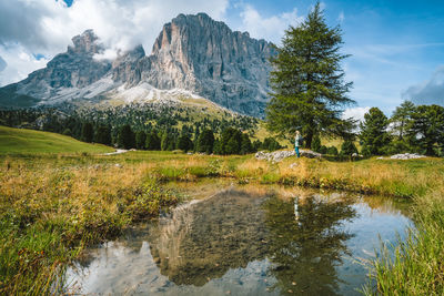 Woman hiking in val gardena. pond and reflection of sassolungo langkofel mountain. dolomites, italy