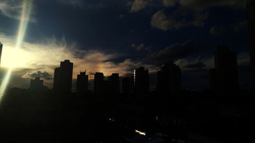 Silhouette of city against cloudy sky during sunset