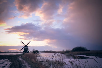 Traditional windmill on shore against sky during sunset