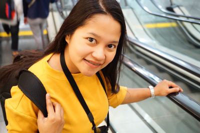 Portrait of smiling teenage girl standing on escalator at railroad station