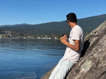Man sitting on rock looking at lake against sky