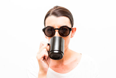 Close-up portrait of young woman holding camera over white background