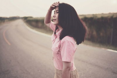 Side view of young woman looking away while standing on road